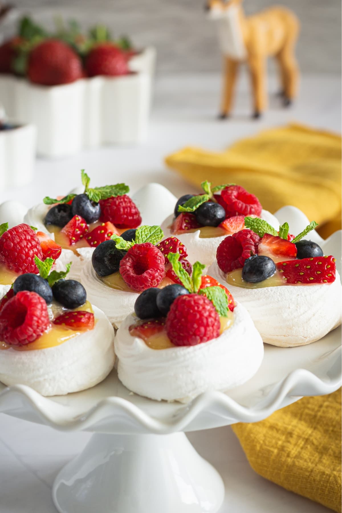 Pavlova topped with custard and berries served on a cake tray.