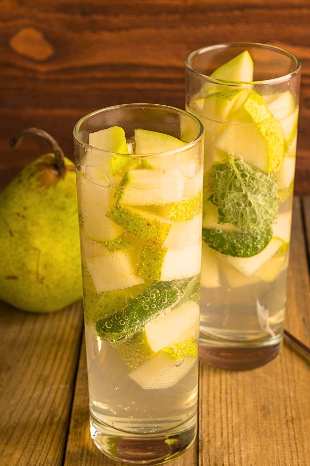 Two glasses of pear vodka cocktail with floating slices of pears garnished with mint. 