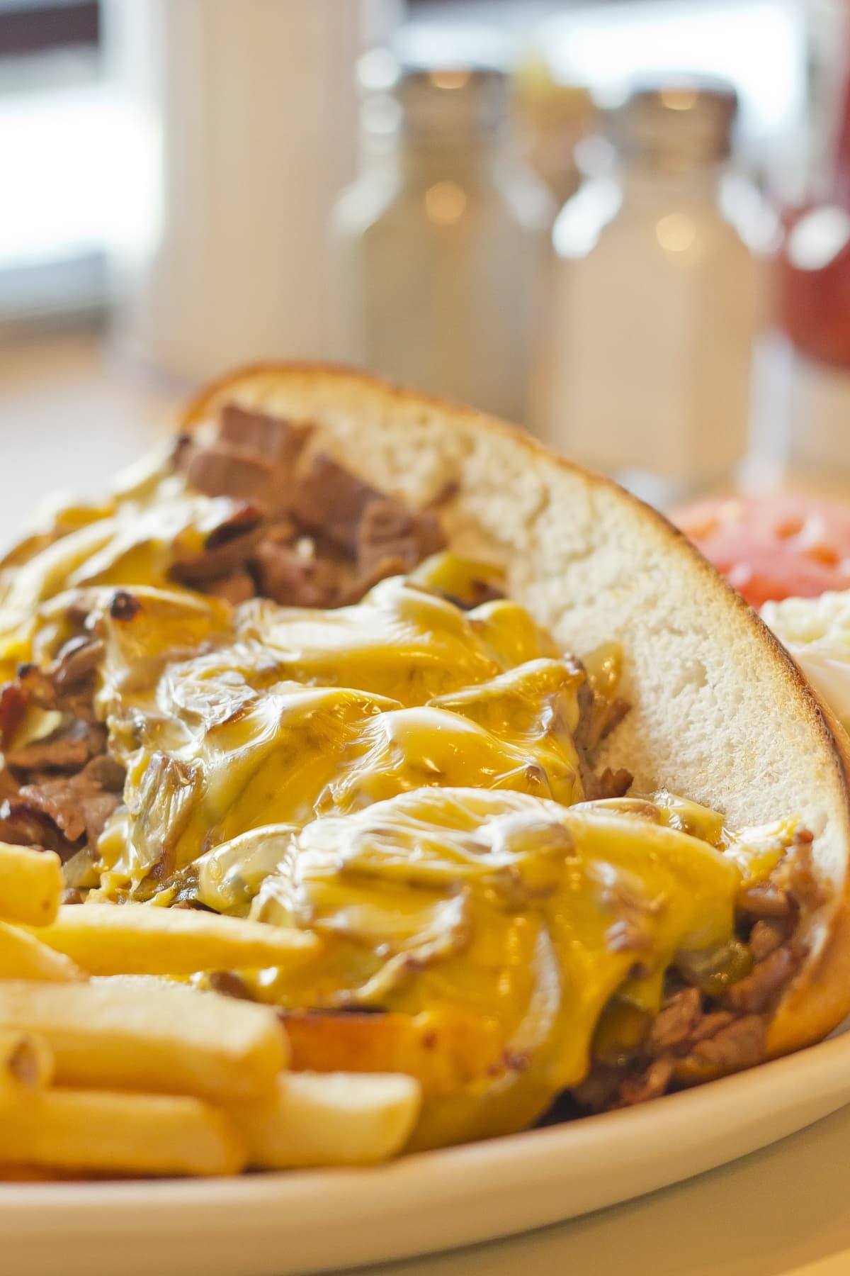 Philly cheesesteak sandwich with cheese sauce served with fries. 
