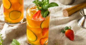 Two glasses of Pimms Cup Cocktail with strawberry, cucumber and lemon slices garnished with mint sprigs.
