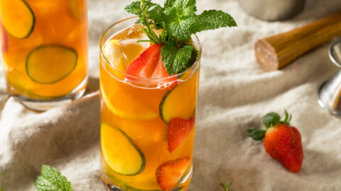 Two glasses of Pimms Cup Cocktail with strawberry, cucumber and lemon slices garnished with mint sprigs.
