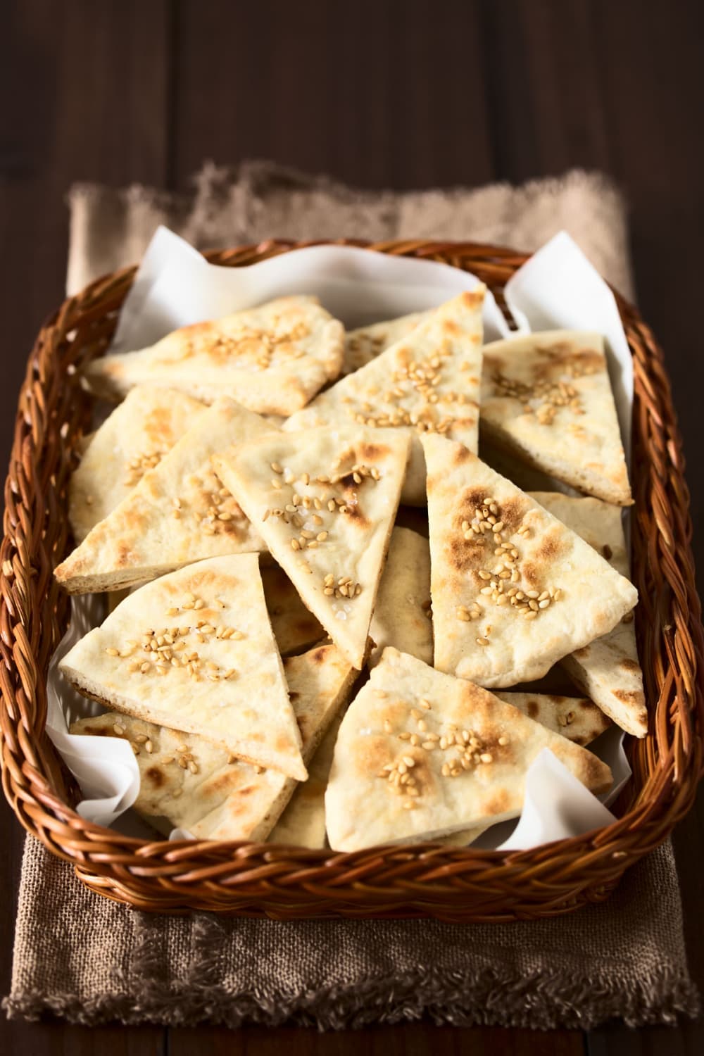 Bunch of triangle shaped pita crackers on a woven basket. 