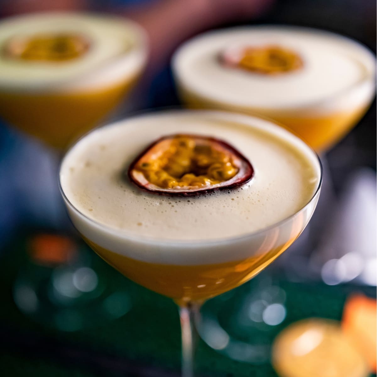 Three glasses of foamy porn star martini with passion fruit slice in half garnish on top. 