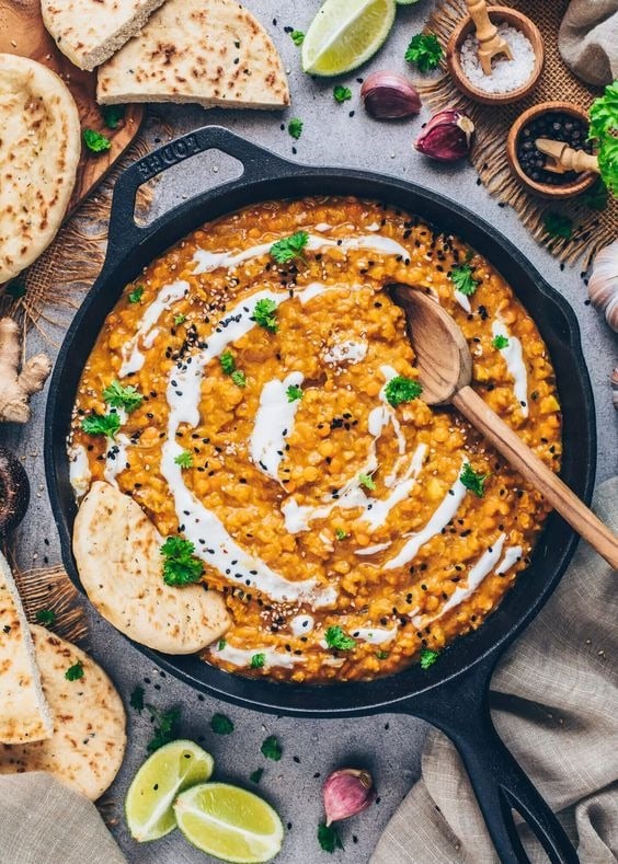 red lentil dal on an iron cast pan drizzled with cream sprinkled with black sesame seeds.