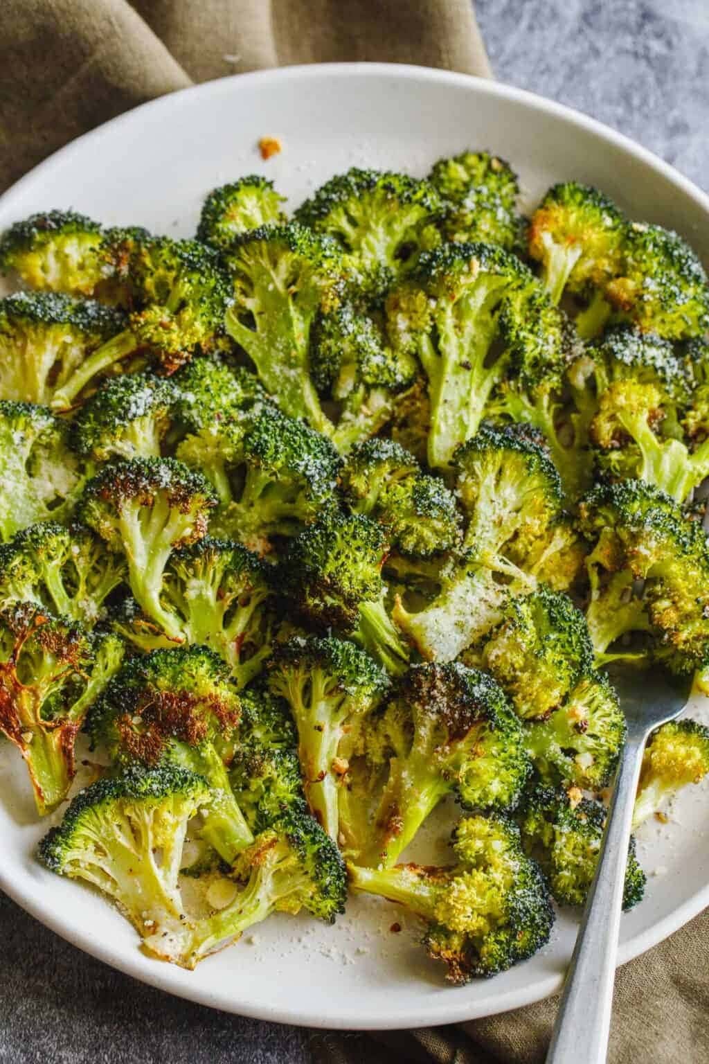 Roasted broccoli served on a white plate with spoon. 