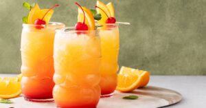 Three glasses of rum punch garnished with orange slices and cherries on stick.