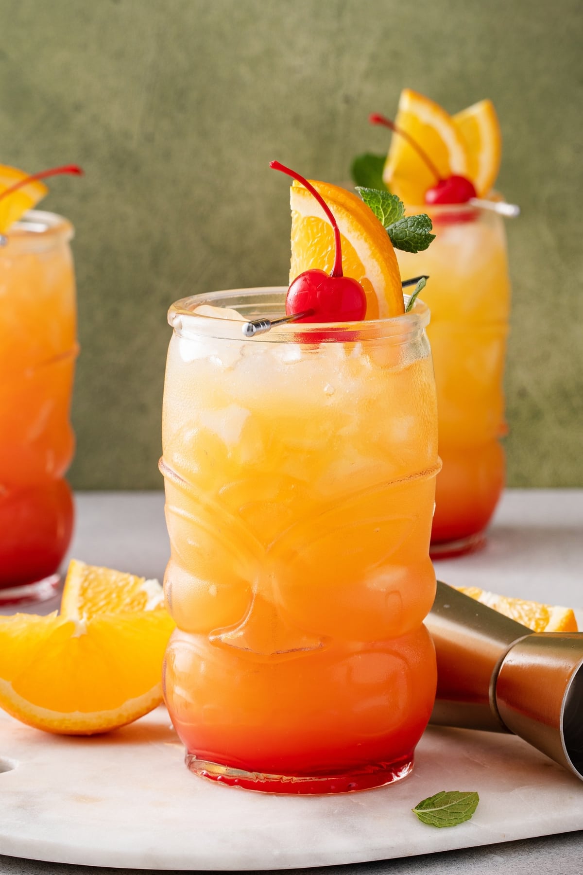 Rum punch served on a tiki glass filled with ice garnished with cherry and orange slice on stick. 