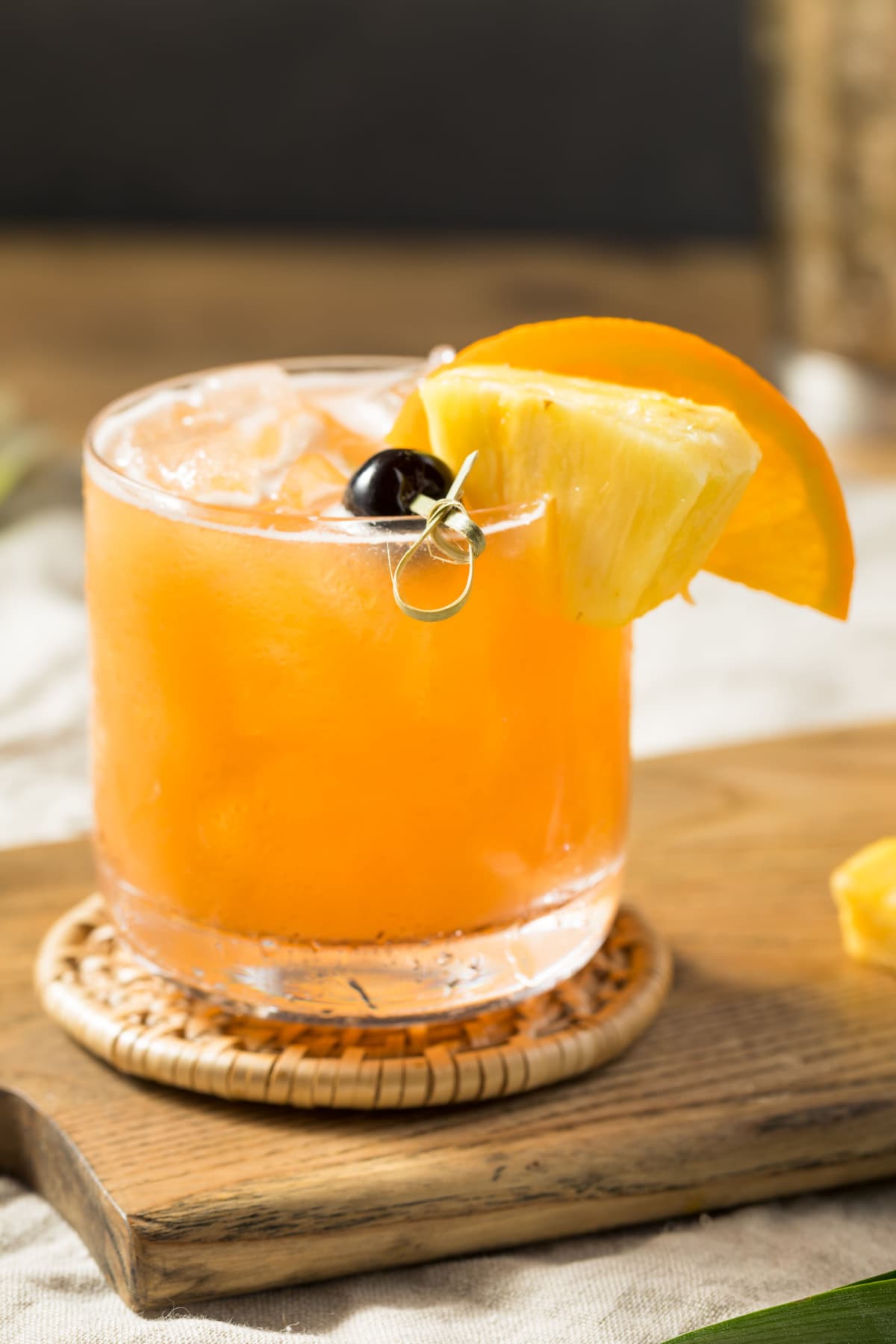Rum runner cocktail on a glass filled with ice garnished with cherry, pineapple slice and orange wheel. 