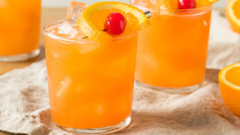 Ice cold rum swizzle cocktails on glass garnish with red cherry and orange peel.