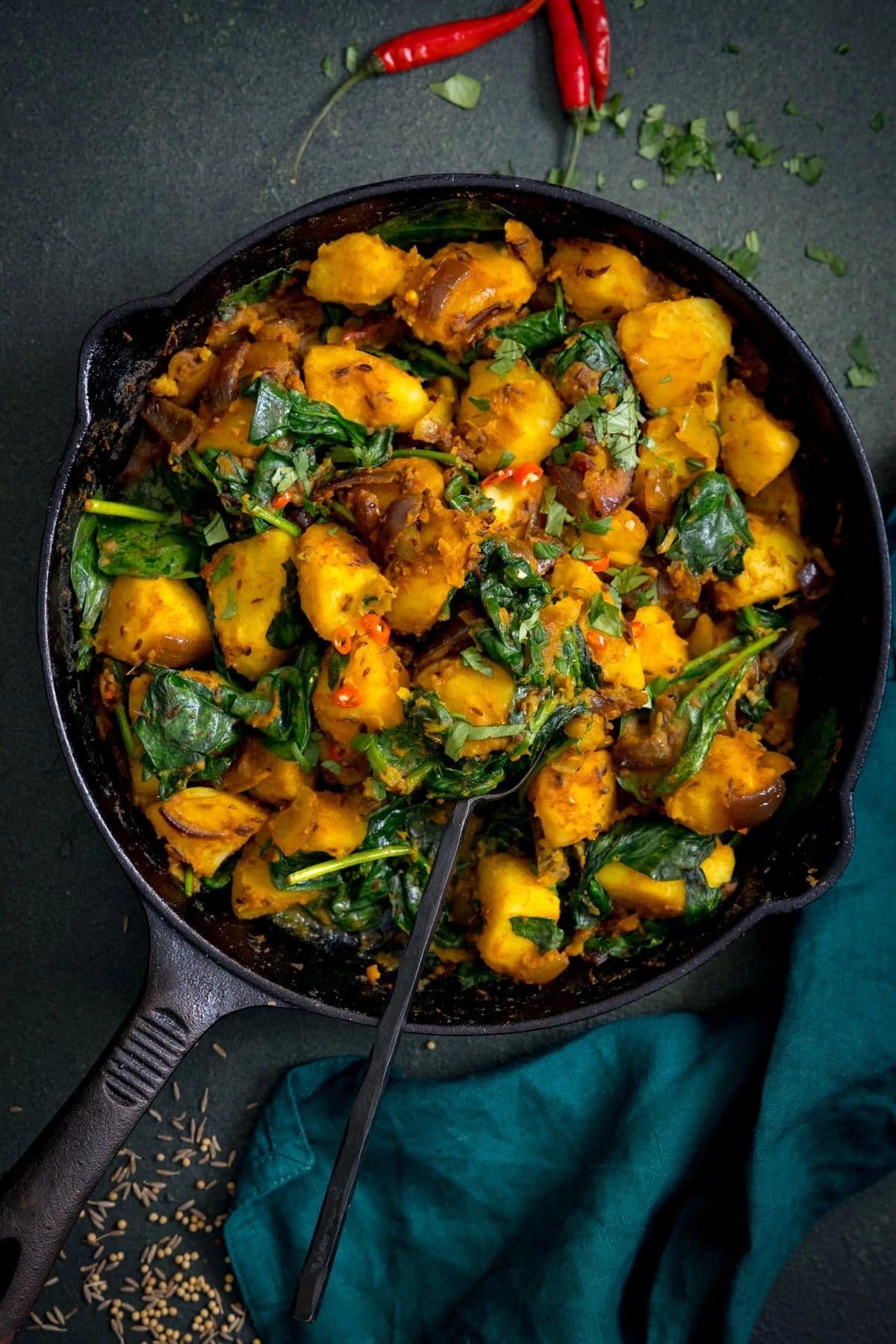Potatoes and spinach mixed on a cast iron pan with seasonings and herbs. 
