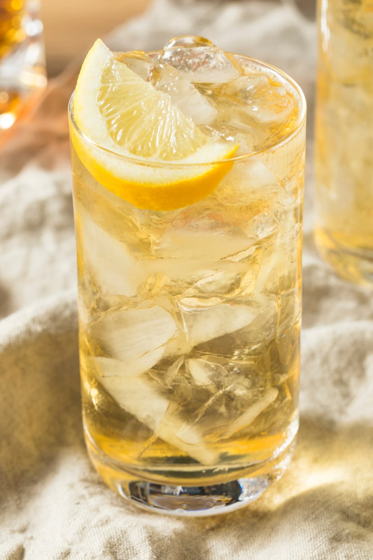 Highball glass filled with ice and seven and seven cocktails garnished with a lemon slice. 