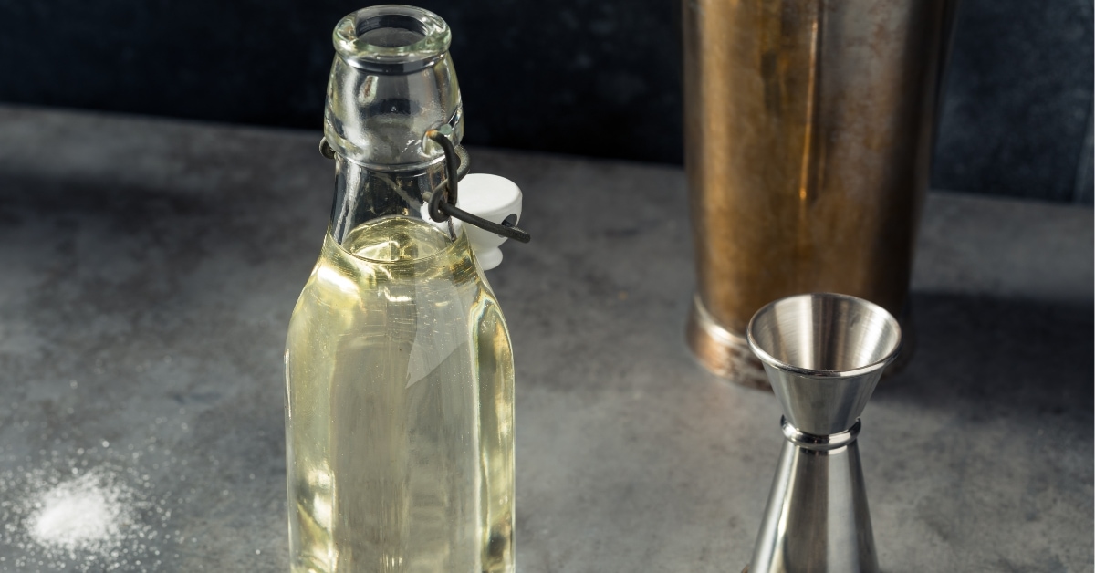 Simple syrup on a glass bottle with shaker and jigger beside.