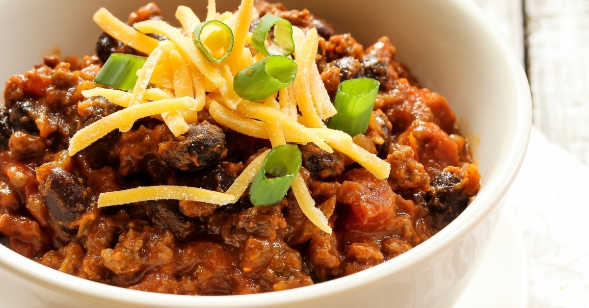 Slow cooker chili in a white bowl topped with grated cheese.