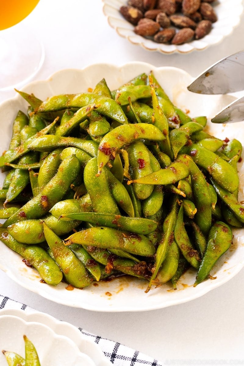 A serving of edamame on a plate sautéed with chili paste, garlic, and miso.