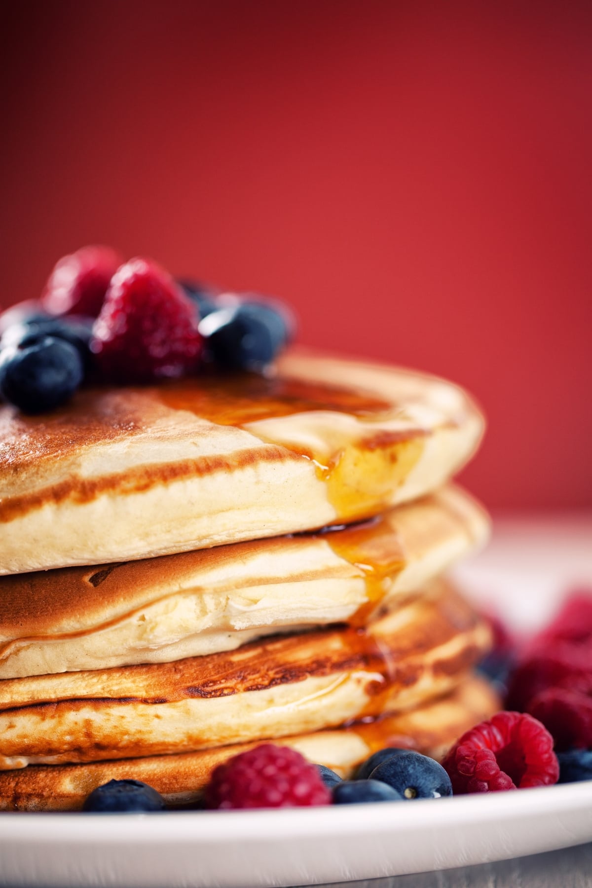 Stack of fluffy Bisquick pancakes drizzled with syrup topped with berries.