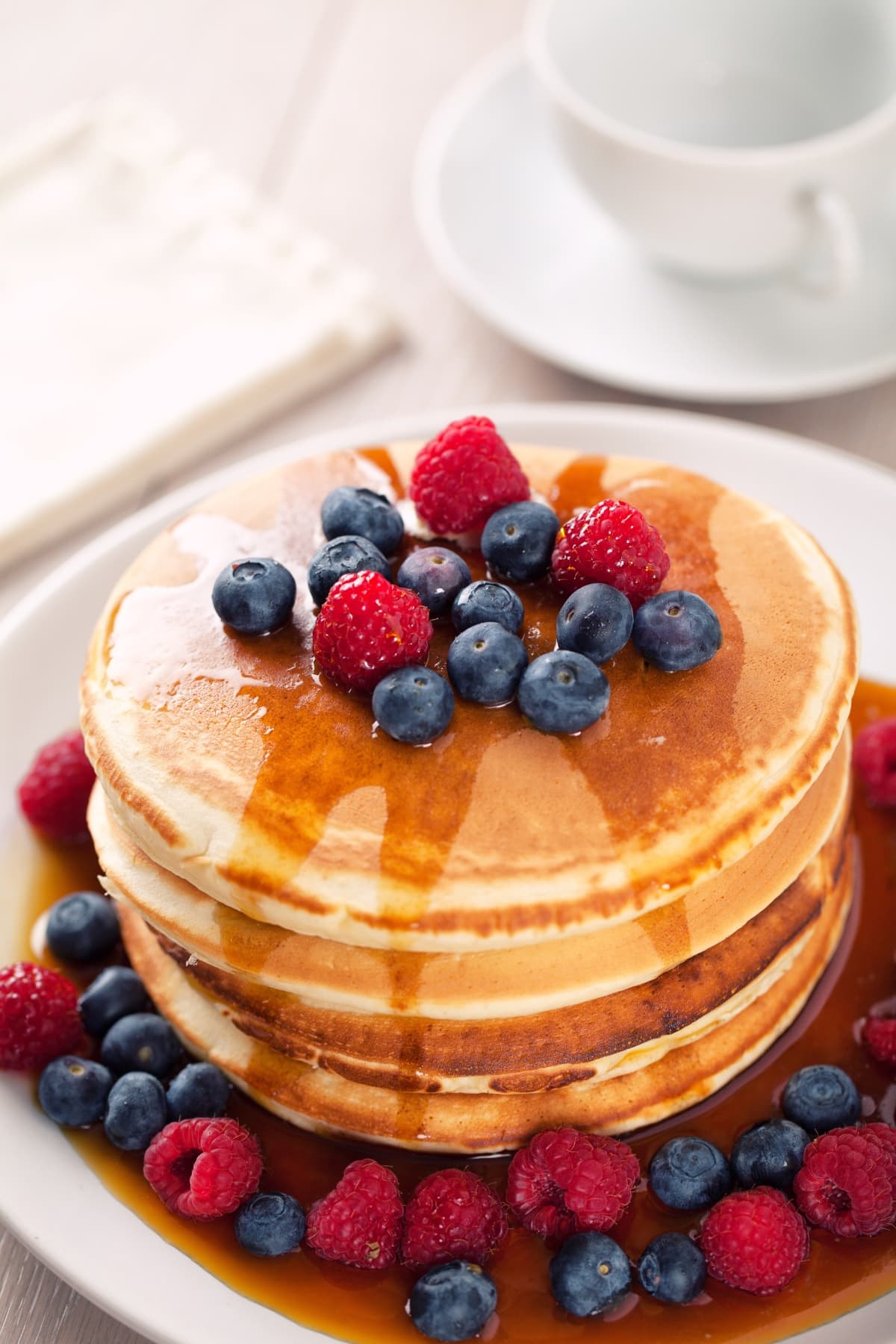 Stack of fluffy Bisquick pancakes topped with berries drizzled with syrup.