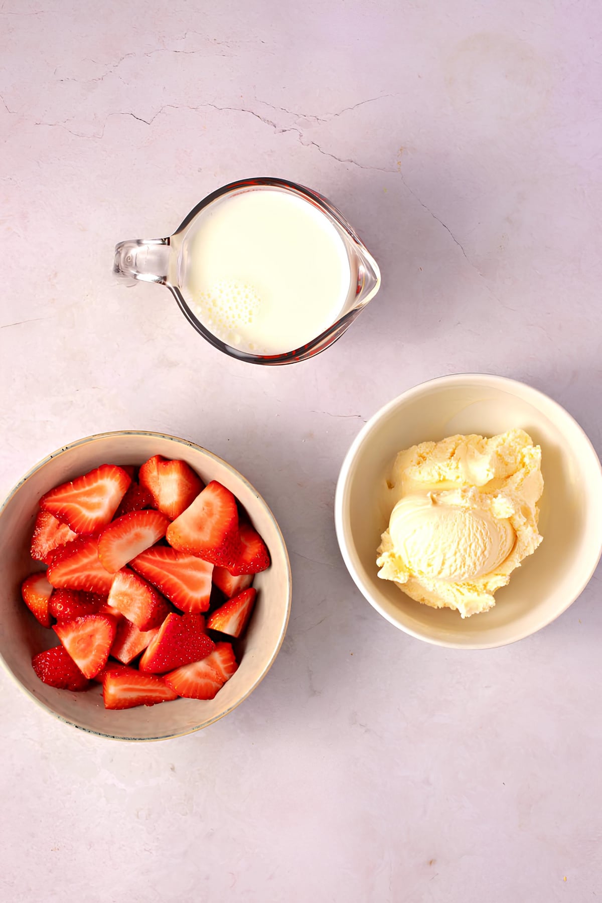Portioned fresh sliced strawberries, whipped cream and milk on a white surface. 