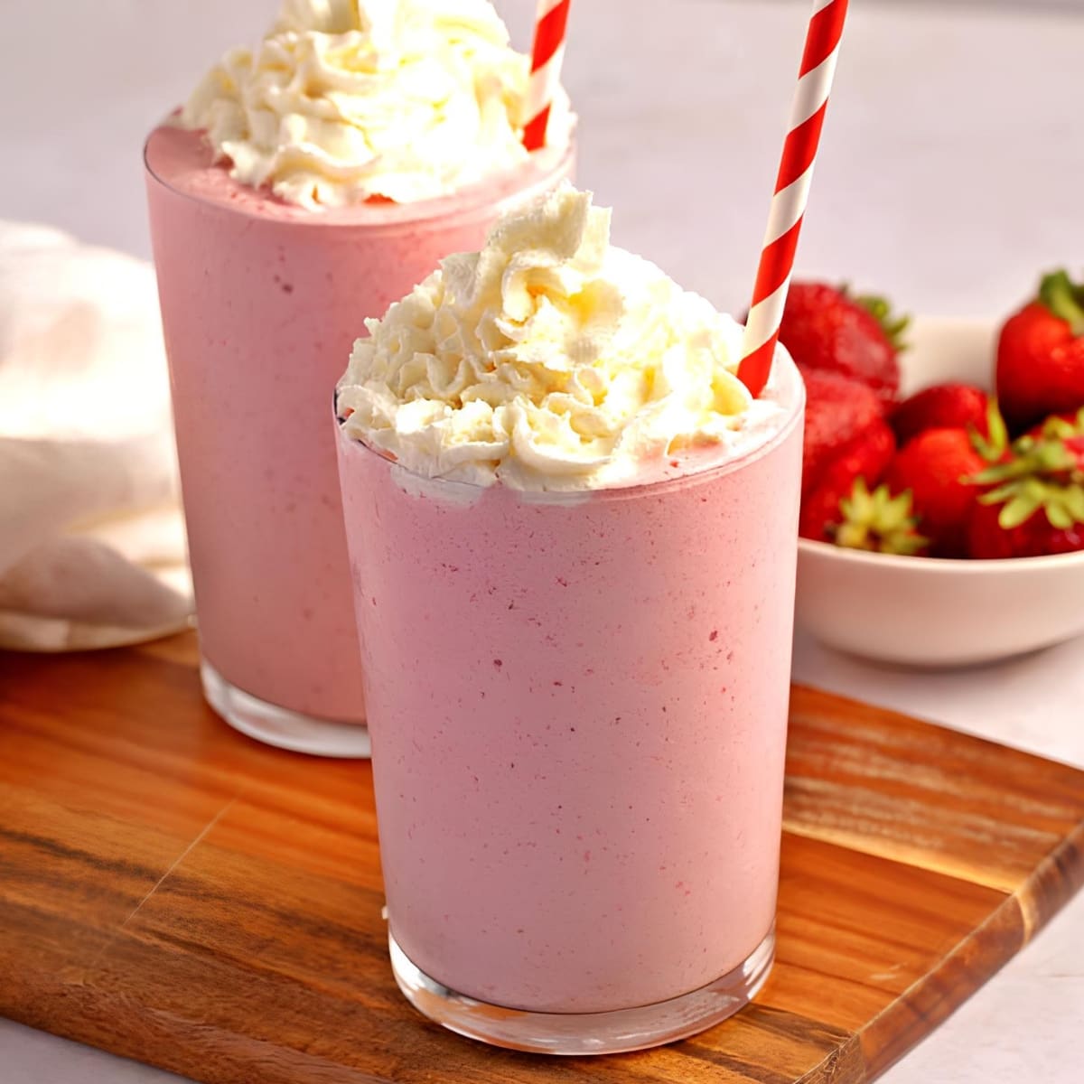 Strawberry smoothie on glasses topped with whipped cream.