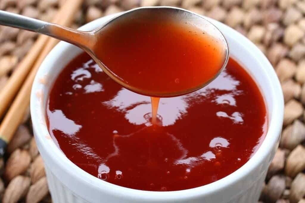 Spoon dripping with sweet and sour sauce form a small bowl. 
