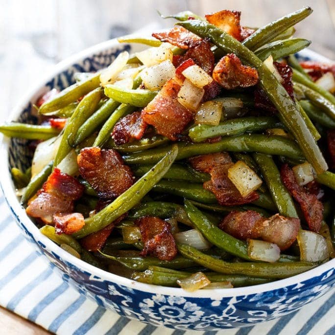A bowl of green beans with sauce and chunks of pork. 
