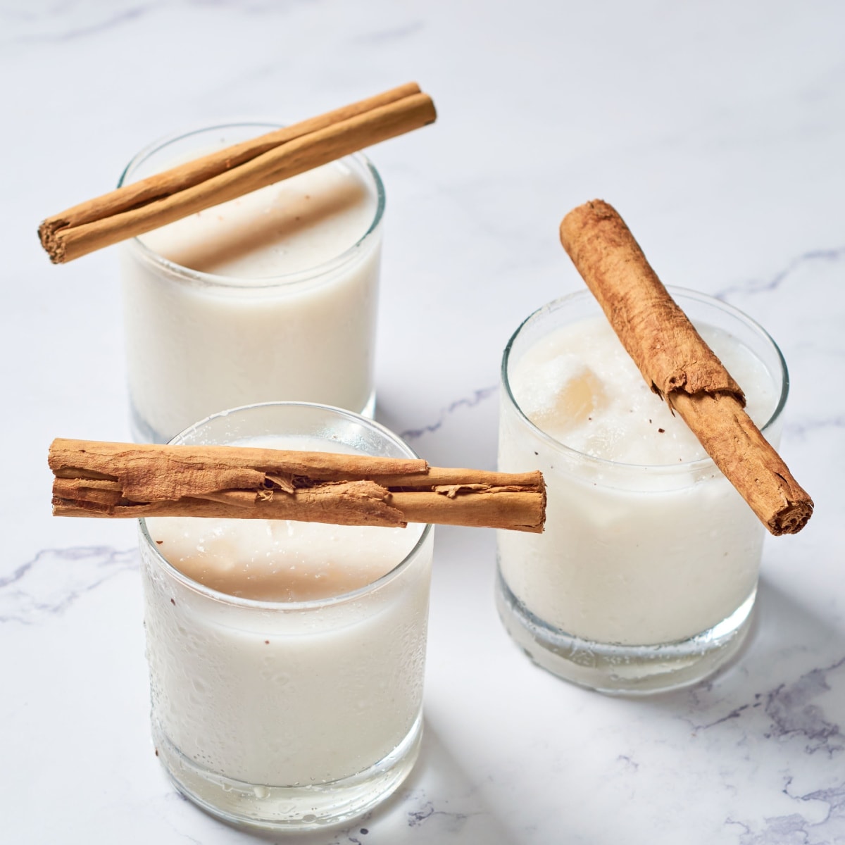 Three glasses of horchata with cinnamon sticks placed on top of each.