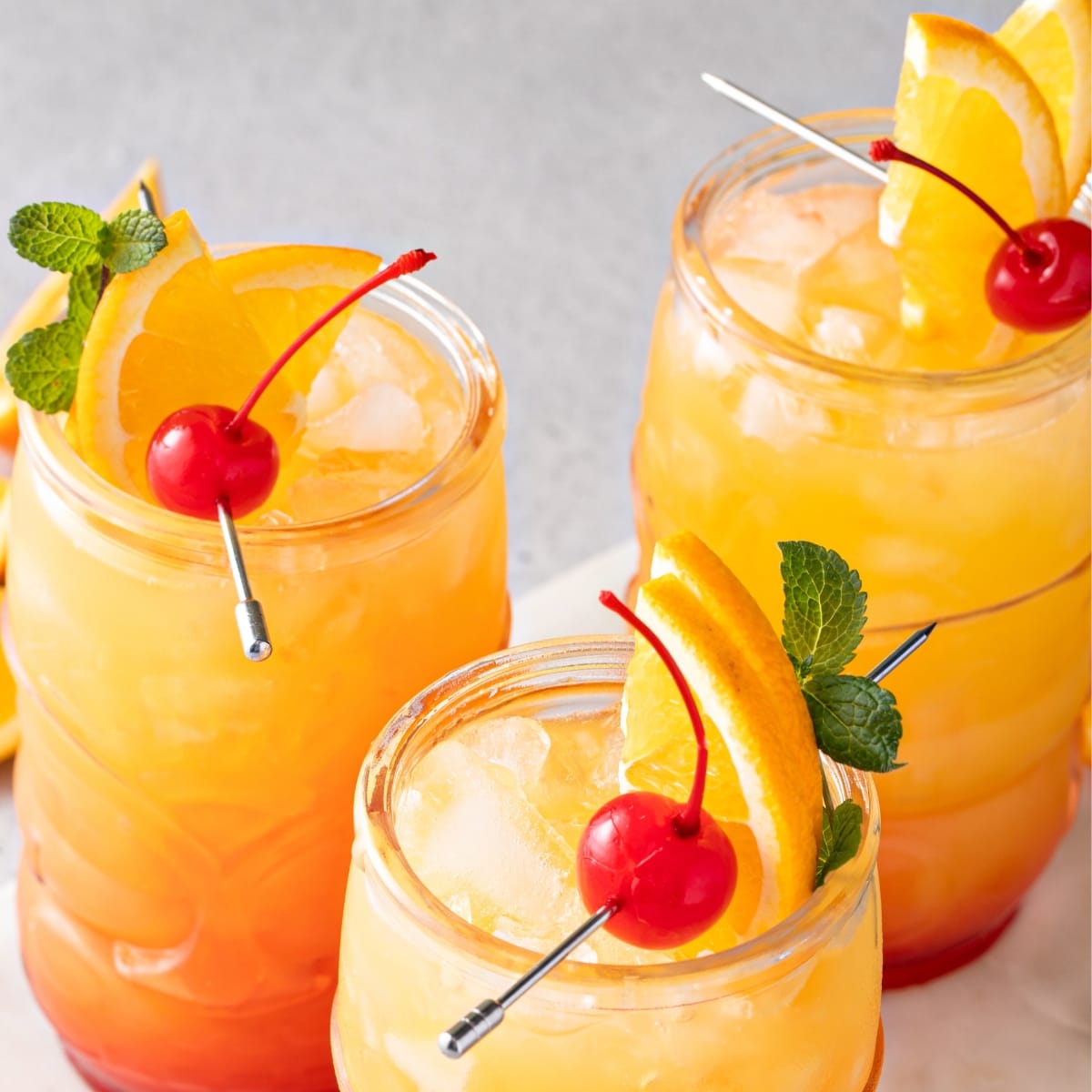 Top view of rum punch on glasses filled with ice garnished with cherries and slices of orange. 