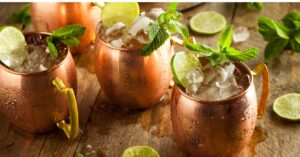 Three mugs of Moscow mule garnished with mint and lemon wheel.