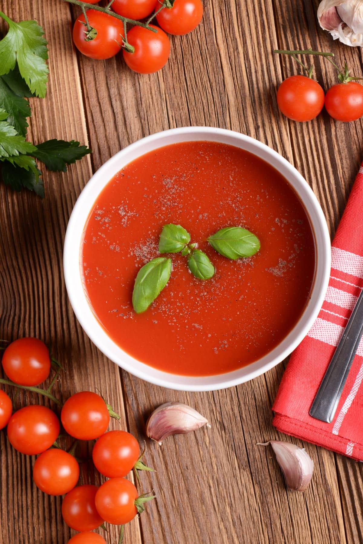 Tomato soup served in a white bowl sprinkled with pepper garnished with basil leaves. 