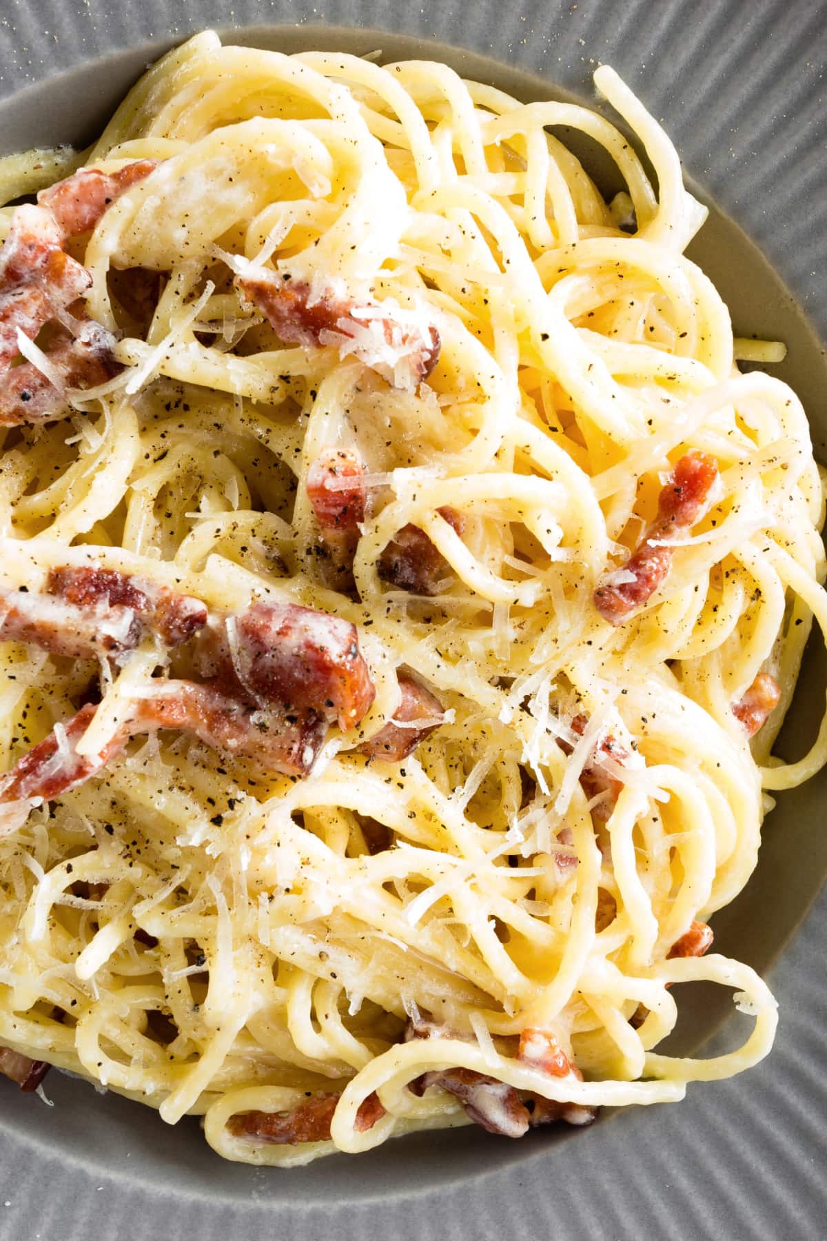 Closeup of a serving of pasta carbonara with bacon and cheese sprinkled with pepper. 
