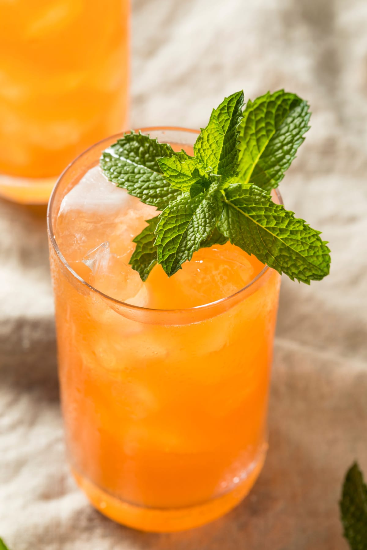 Closeup of orange colored cocktail filled on a tall glass filled with ice.