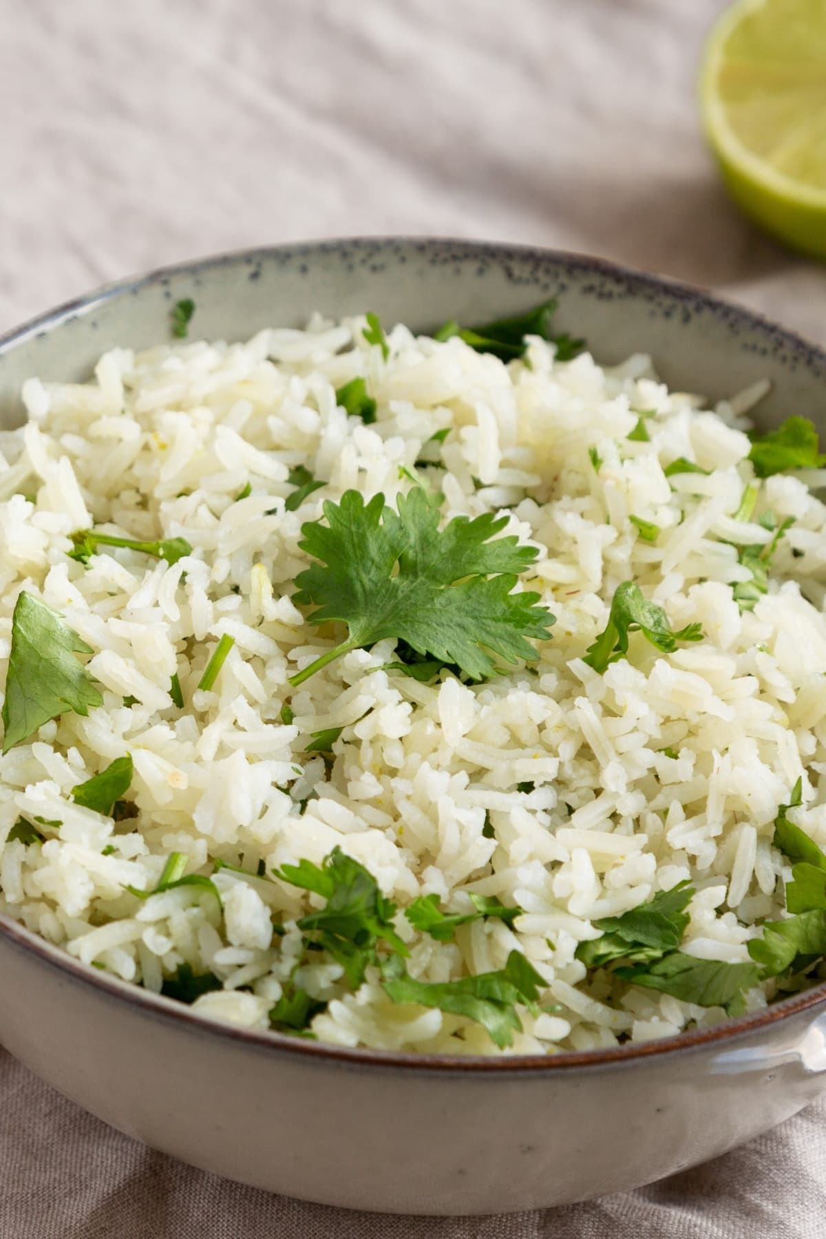 Closeup of cooked rice in a bowl with lime and cilantro leaves.