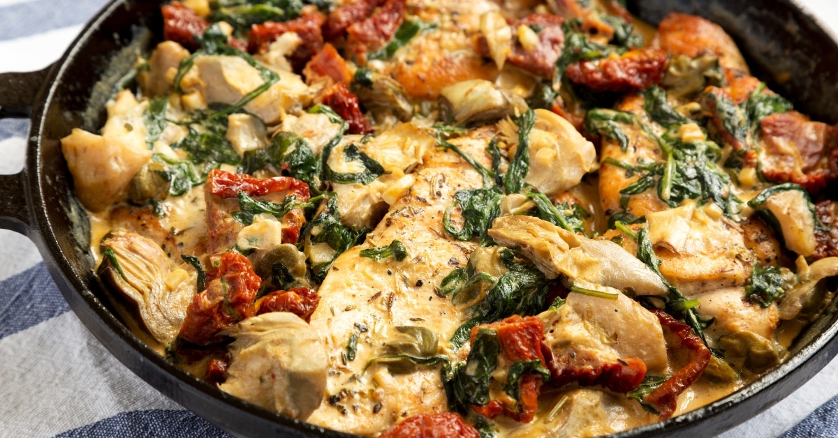 A skillet with tuscan chicken, spinach and sun-dried tomatoes
