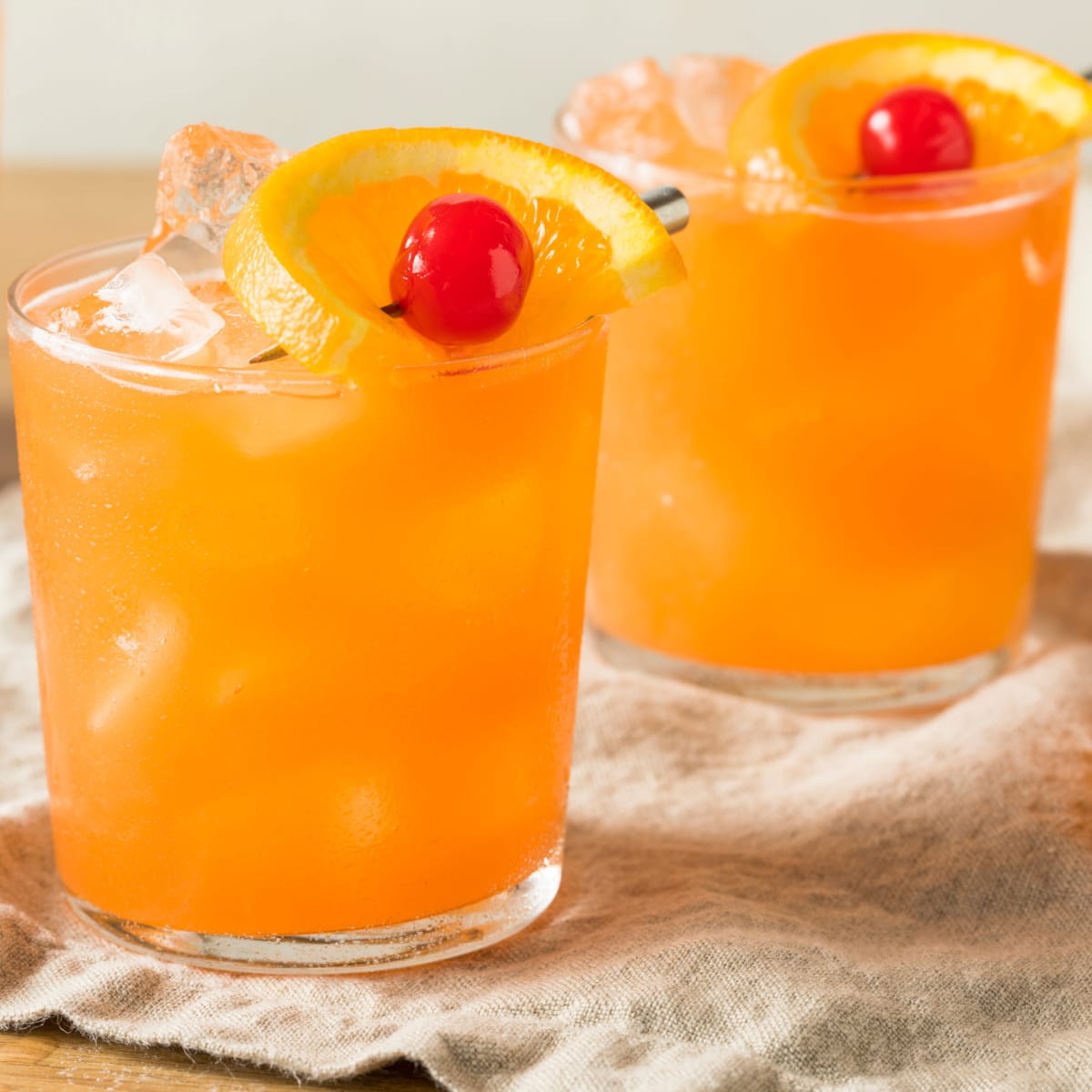 Two glasses serving of rum swizzle filed with ice on top of a cloth. 