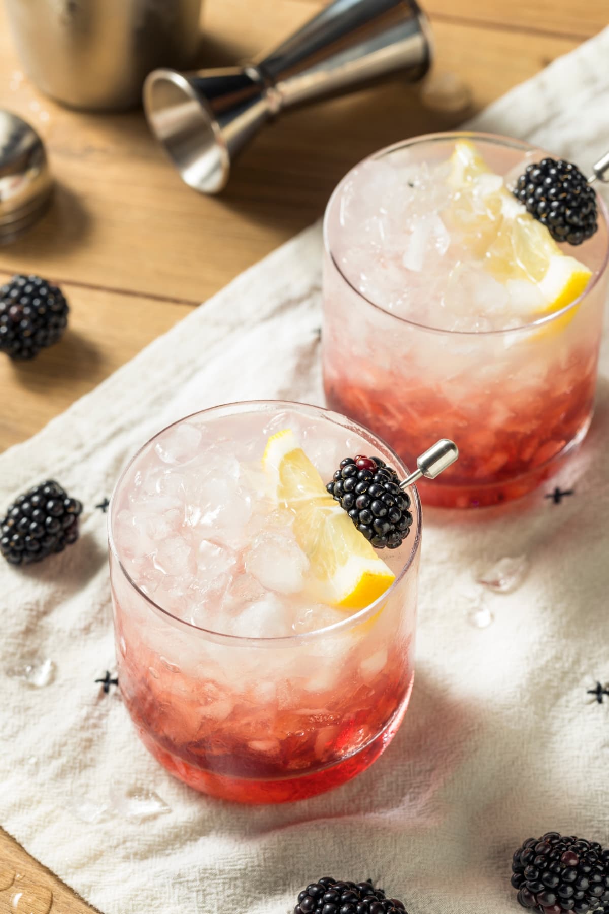 Bramble cocktail served in glasses filled with crushed ice garnished with blackberries on skewers and a slice of lemon. 
