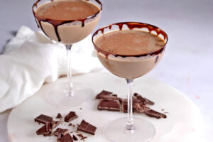 Two glasses of chocolate martini in cocktail glasses and chocolate shaving on tray.