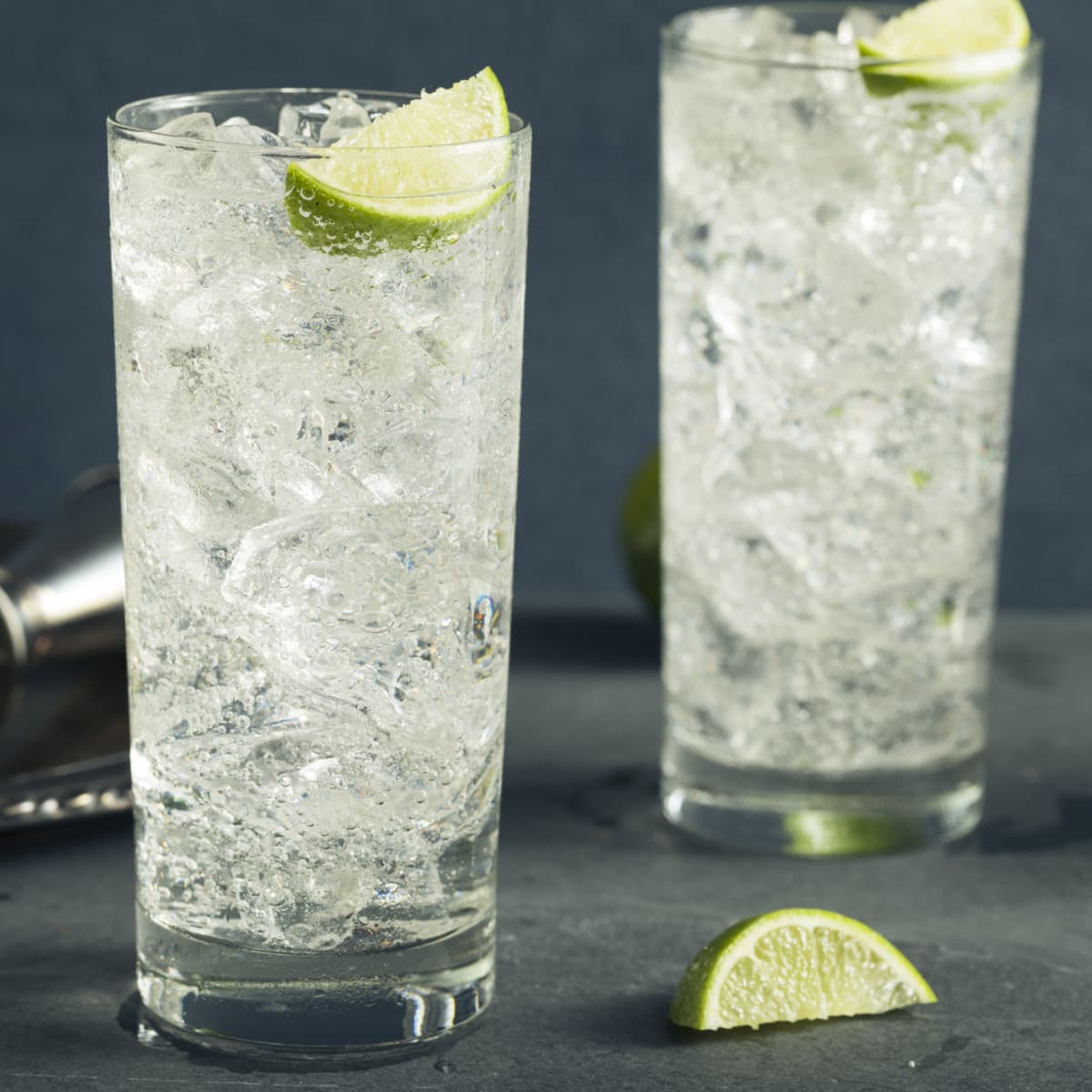 Two tall glasses of vodka soda filled with ice garnished with lime slice.