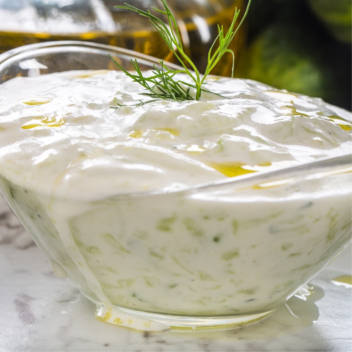 Tzatziki sauce on a glass boat shape bowl garnished with fresh dill leaves on top.