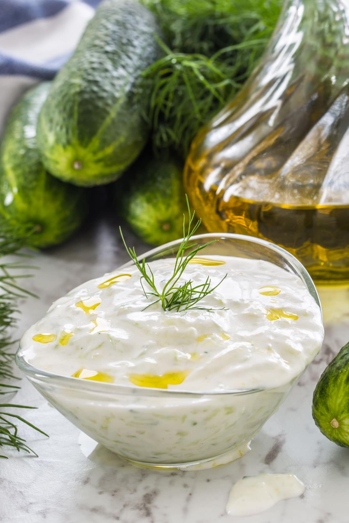 Boat shaped glass bowl overflowing with tzatziki sauce garnished with fresh dill leaves and drizzle of olive oil.