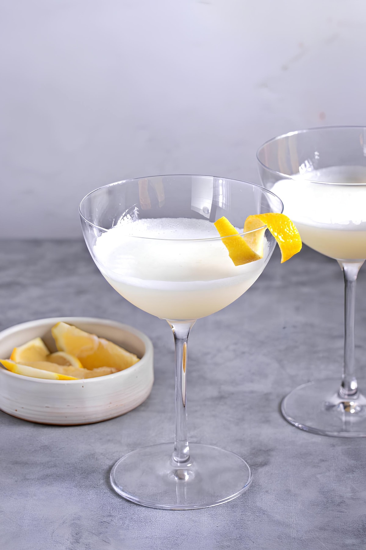 Two glasses of white lady cocktail garnished with lemon twist. 