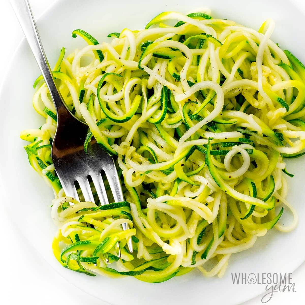 Zucchini noodles served on a white plate with fork. 