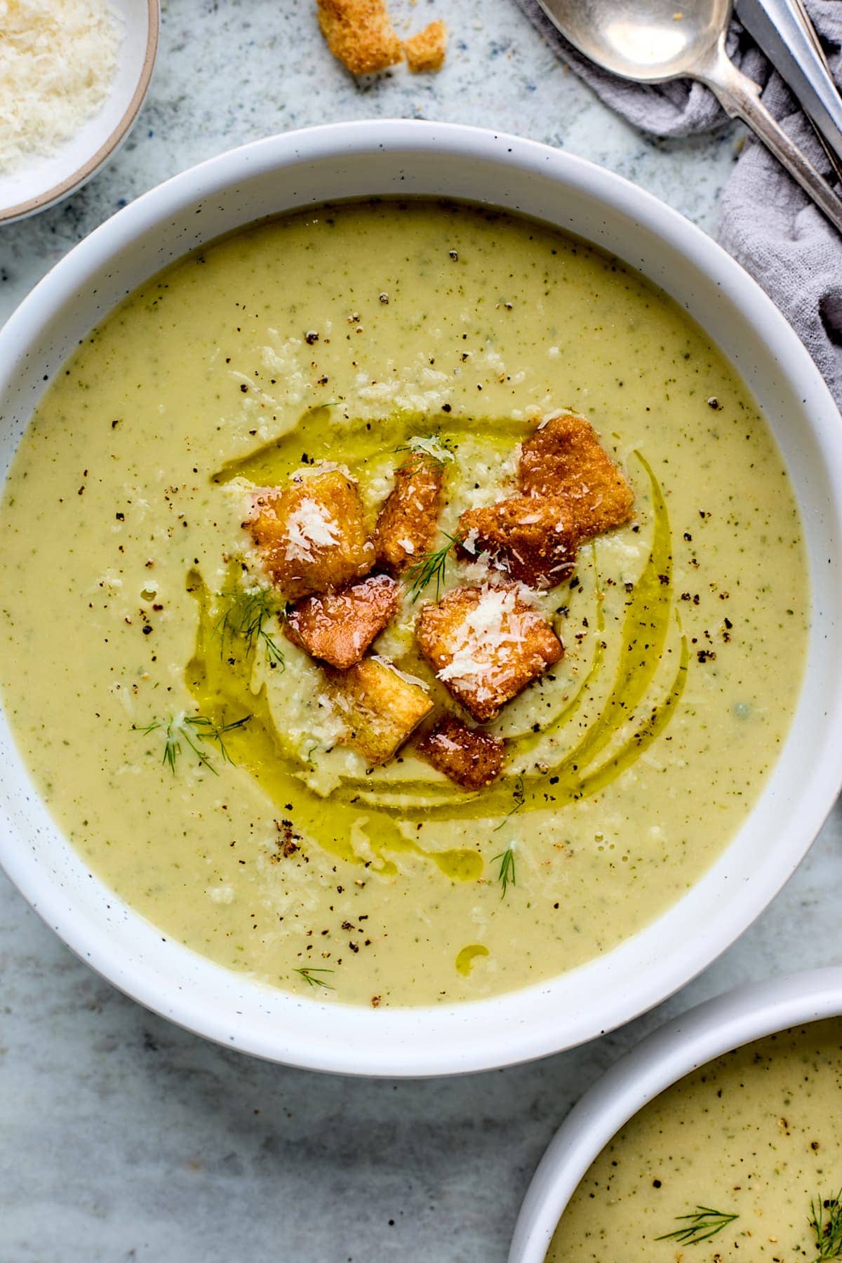 Creamy zucchini soup in a bowl with beans, onion, garlic and lemon, topped with oil and croutons