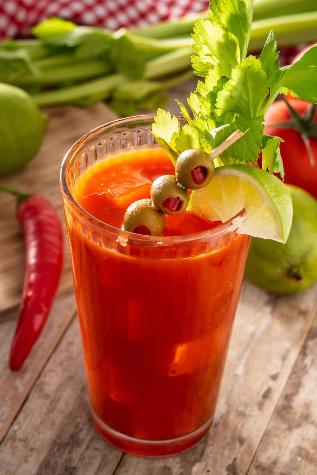 Bloody Mary Cocktail Recipe: A glass of Bloody Mary with fresh tomato, chili. lime and celery on a wooden table