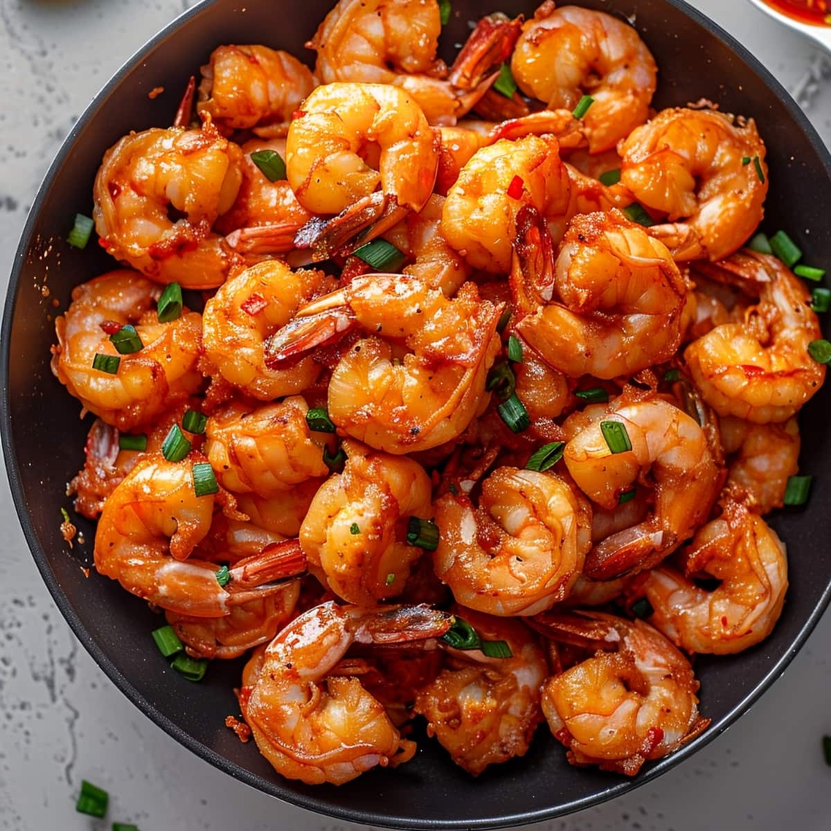 Firecracker shrimp with chopped green onions in a black bowl