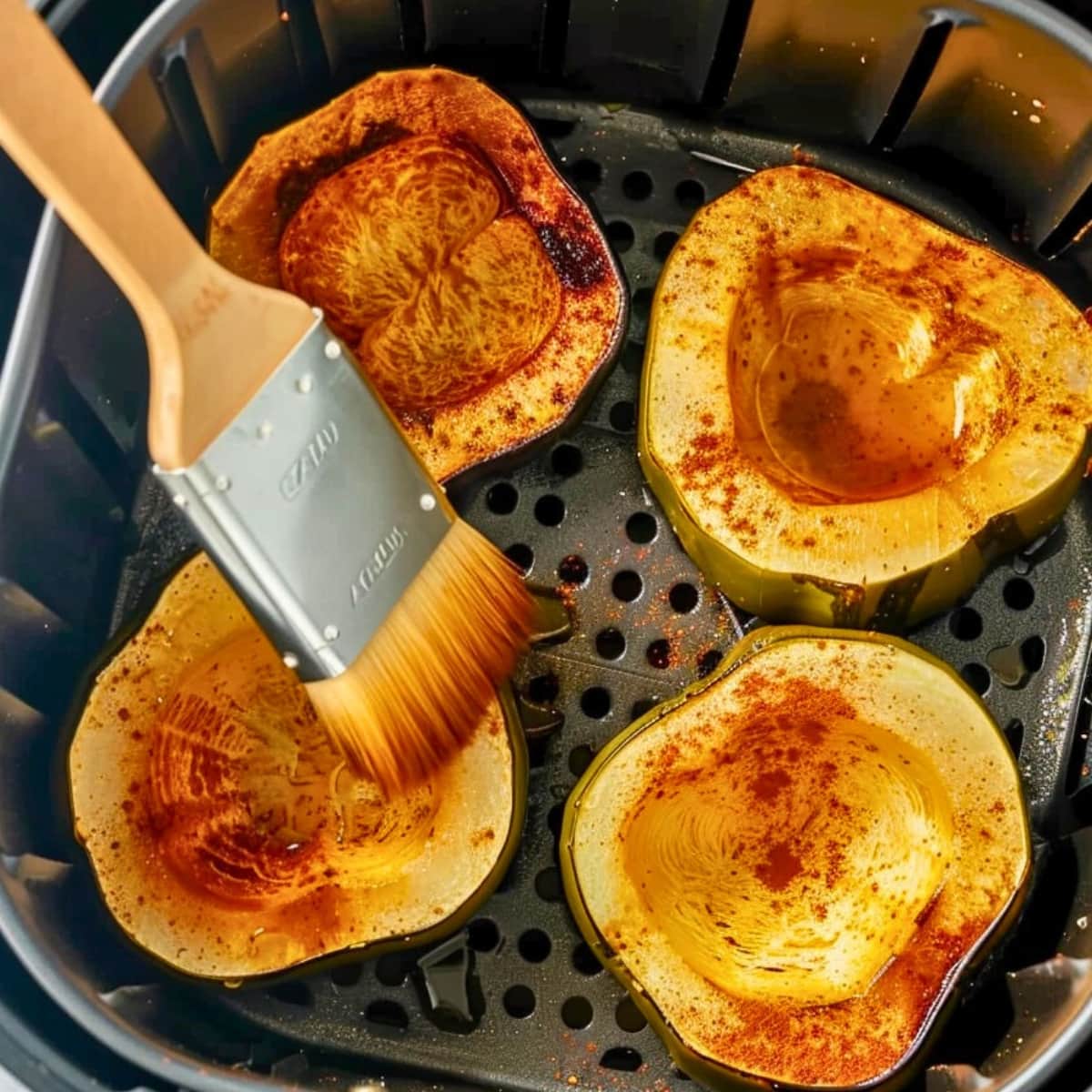 Sliced acorn squash brushed with olive oil with the brown sugar, cinnamon, salt, and pepper mixture inside an air fryer basket.