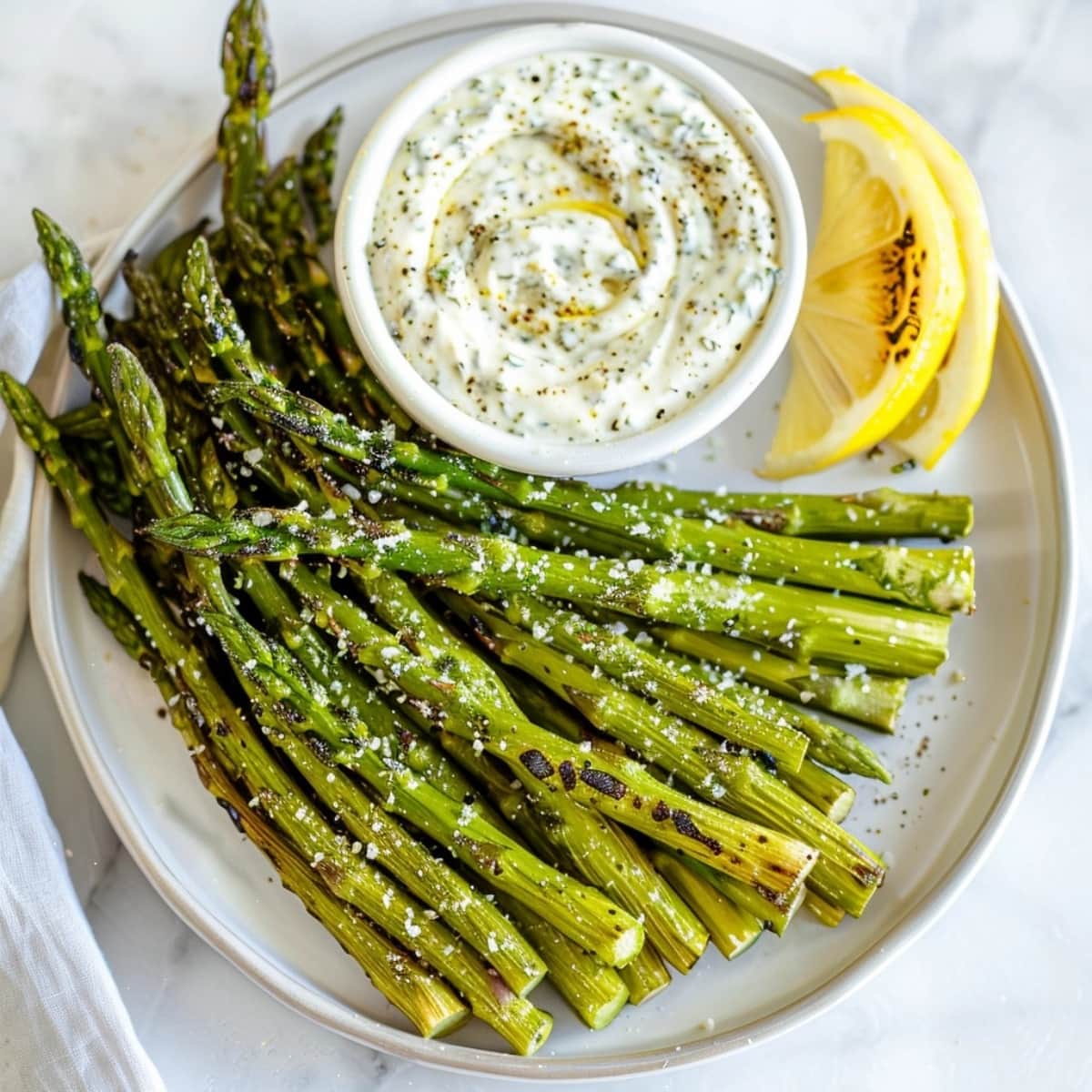 Seasoned air fried asparagus served with dip and lemon slices.