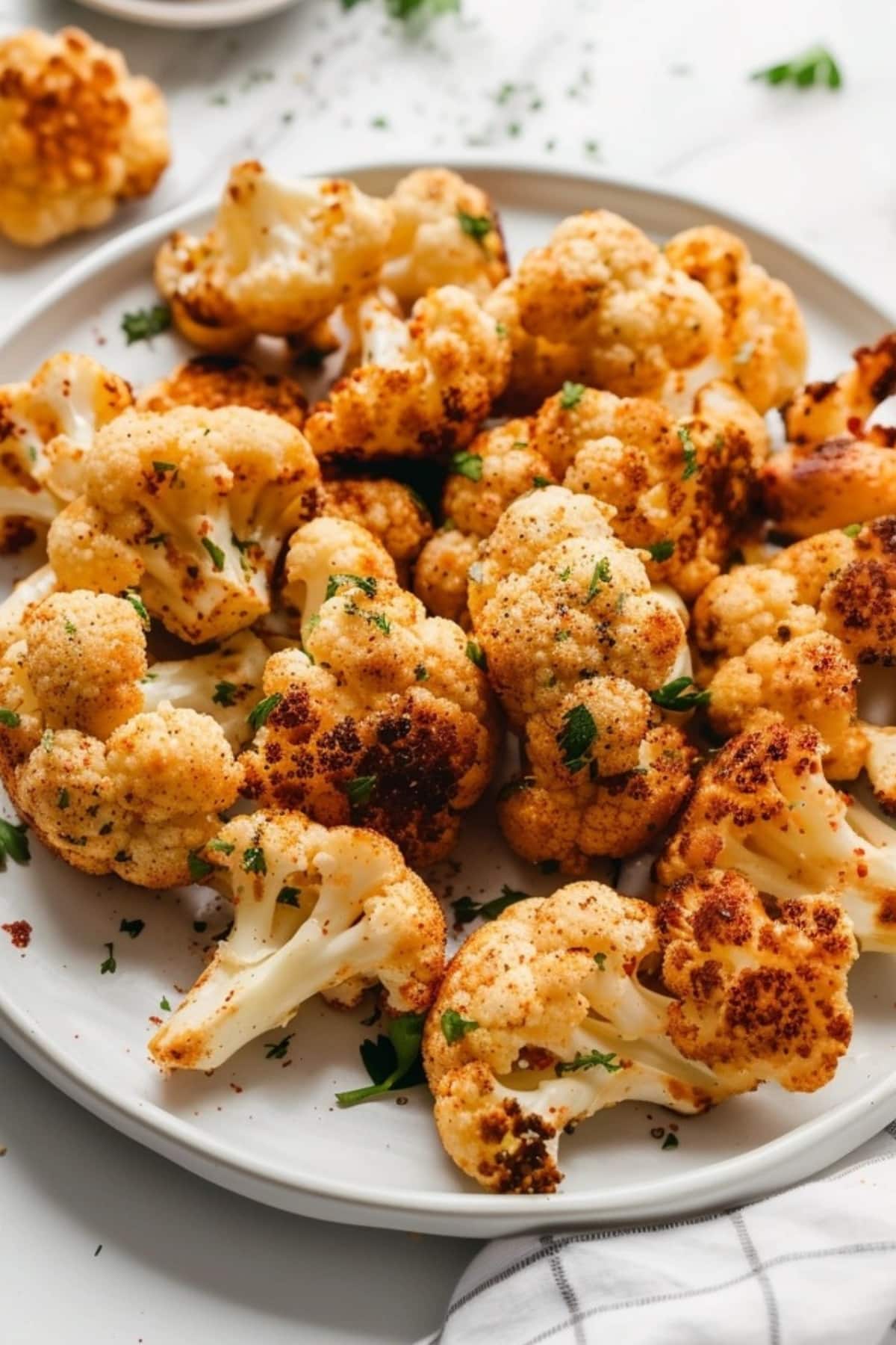 Air fried cauliflower florets served on a white plate garnished with chopped parsley.