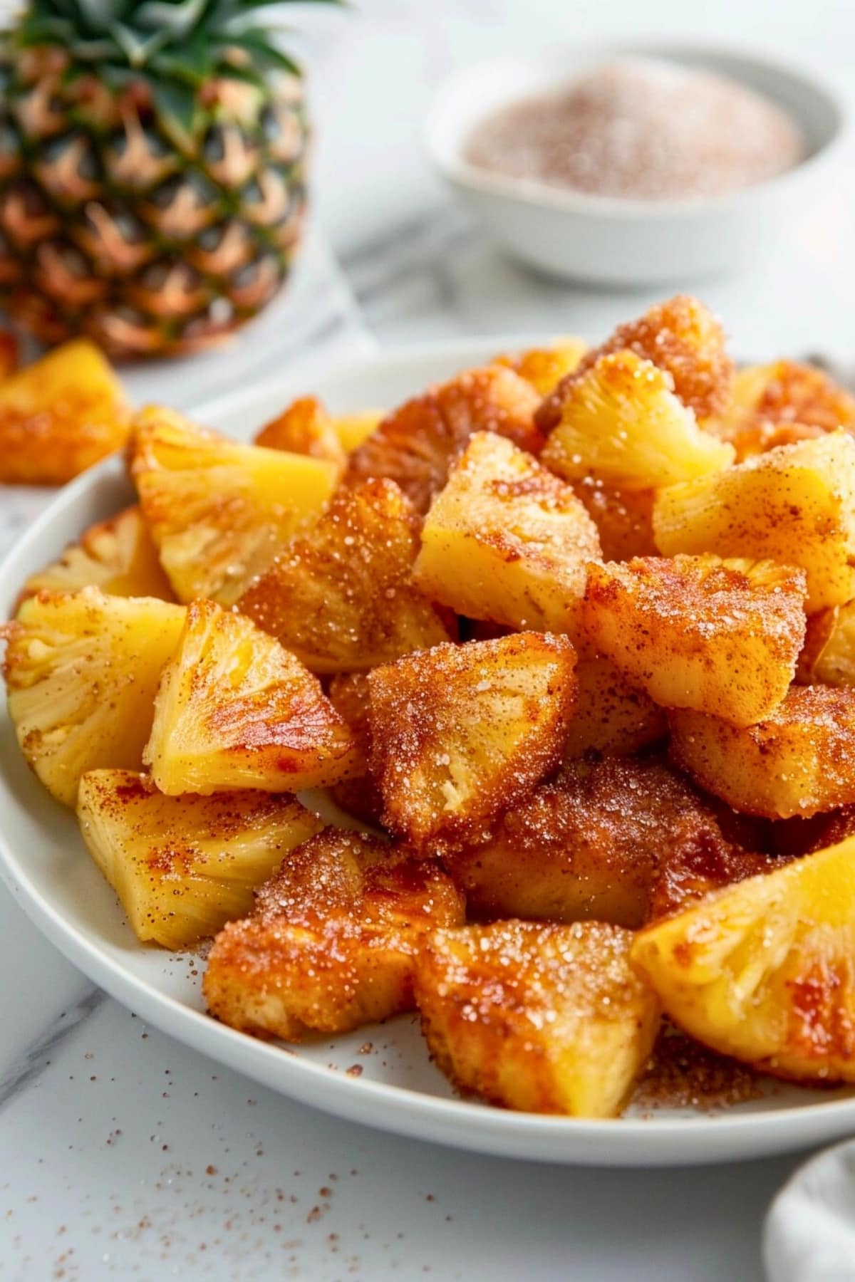 Bite size air fried cinnamon sugar coated pineapple in a white plate.