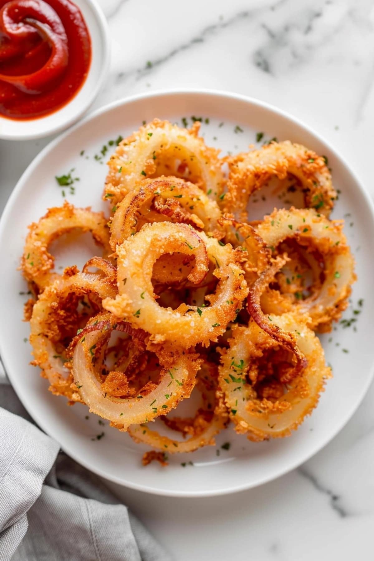 Bunch of air fried onion rings in a plate garnished with chopped herbs.