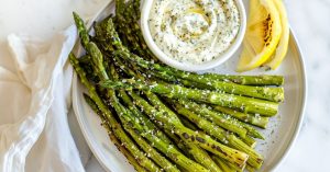 Air fried asparagus sprinkled with parmesan cheese in a plate served with ranch dip.