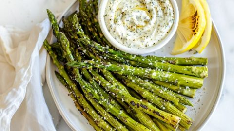 Air fried asparagus sprinkled with parmesan cheese in a plate served with ranch dip.